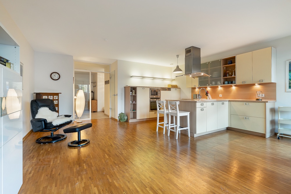 Helle Wohnküche mit Holzfußboden, offener Einbauküche und Sitzecke mit Sessel und Lampe.