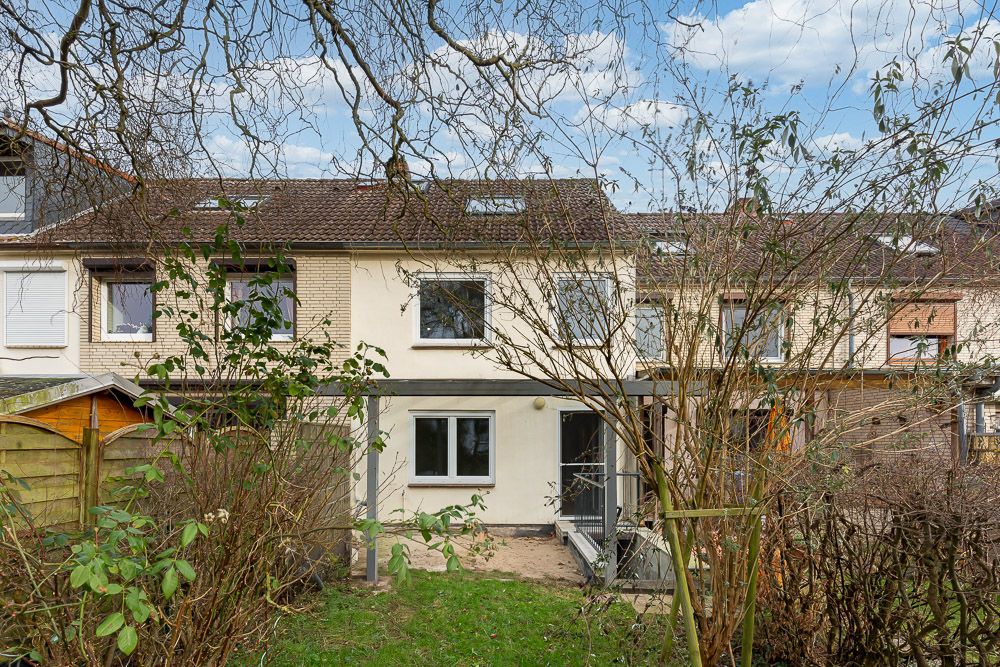 Rückseite eines Reihenhauses mit Garten, Terrasse und Bäumen im Vordergrund.