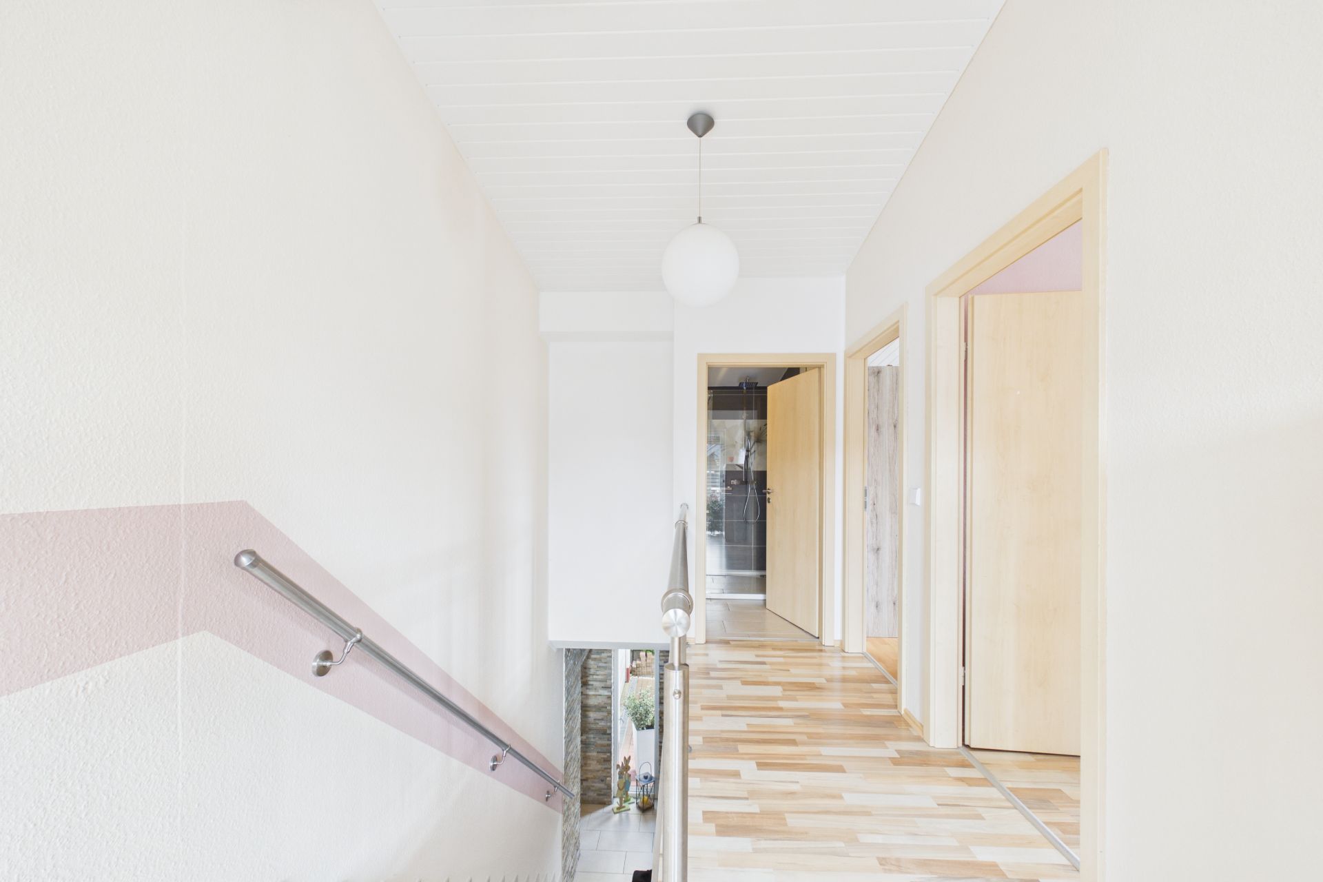 Heller Flur mit Holzfußboden, drei offenen Zimmertüren und Treppenabgang.