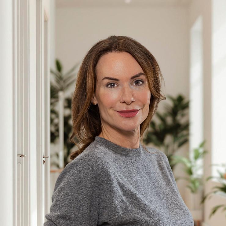 Frau steht in hellem Raum mit Holzboden und vielen grünen Pflanzen.