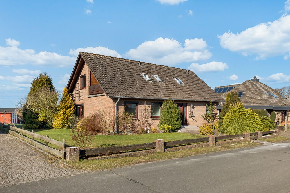 Zweistöckiges Einfamilienhaus mit Garten, Ziegelmauerwerk und Satteldach, von Zaun und Büschen umgeben.