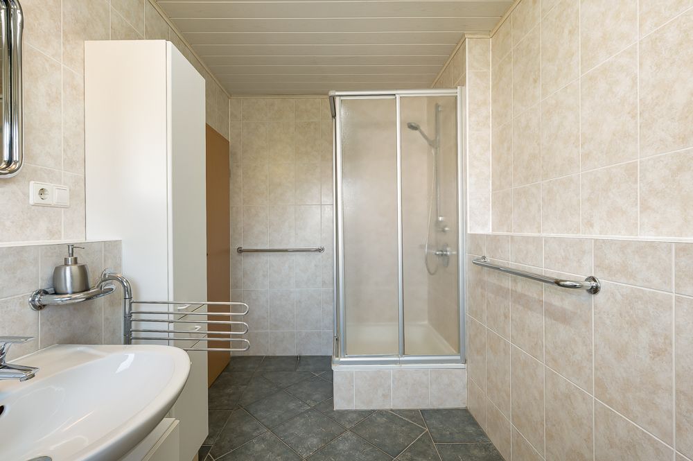 Modernes Badezimmer mit Dusche, Waschbecken, Handtuchhalter und hellen Fliesen.