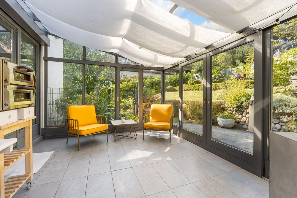 Heller Wintergarten mit zwei gelben Sesseln, kleinem Tisch und großem Fensterblick auf den Garten.