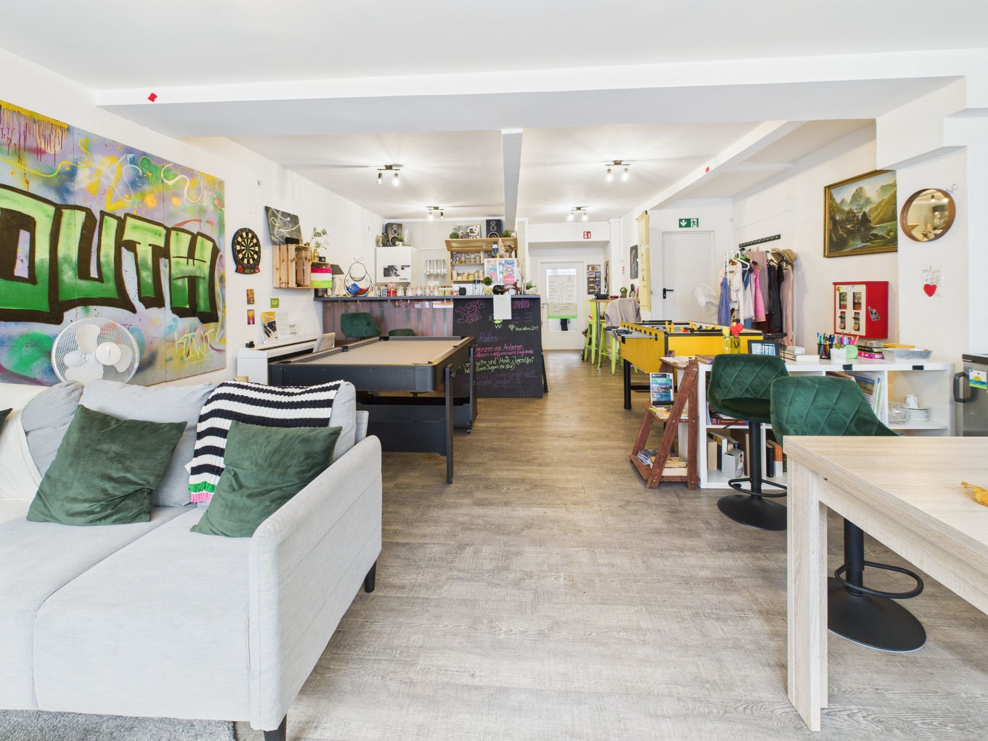 Wohnraum mit Sofa, Billardtisch, Kicker und bunter Wandkunst, helle und offene Gestaltung.