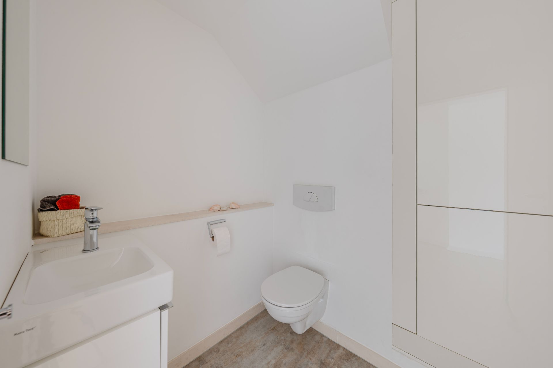 Helles Badezimmer mit Wandtoilette, Waschbecken und weißem Schrank.