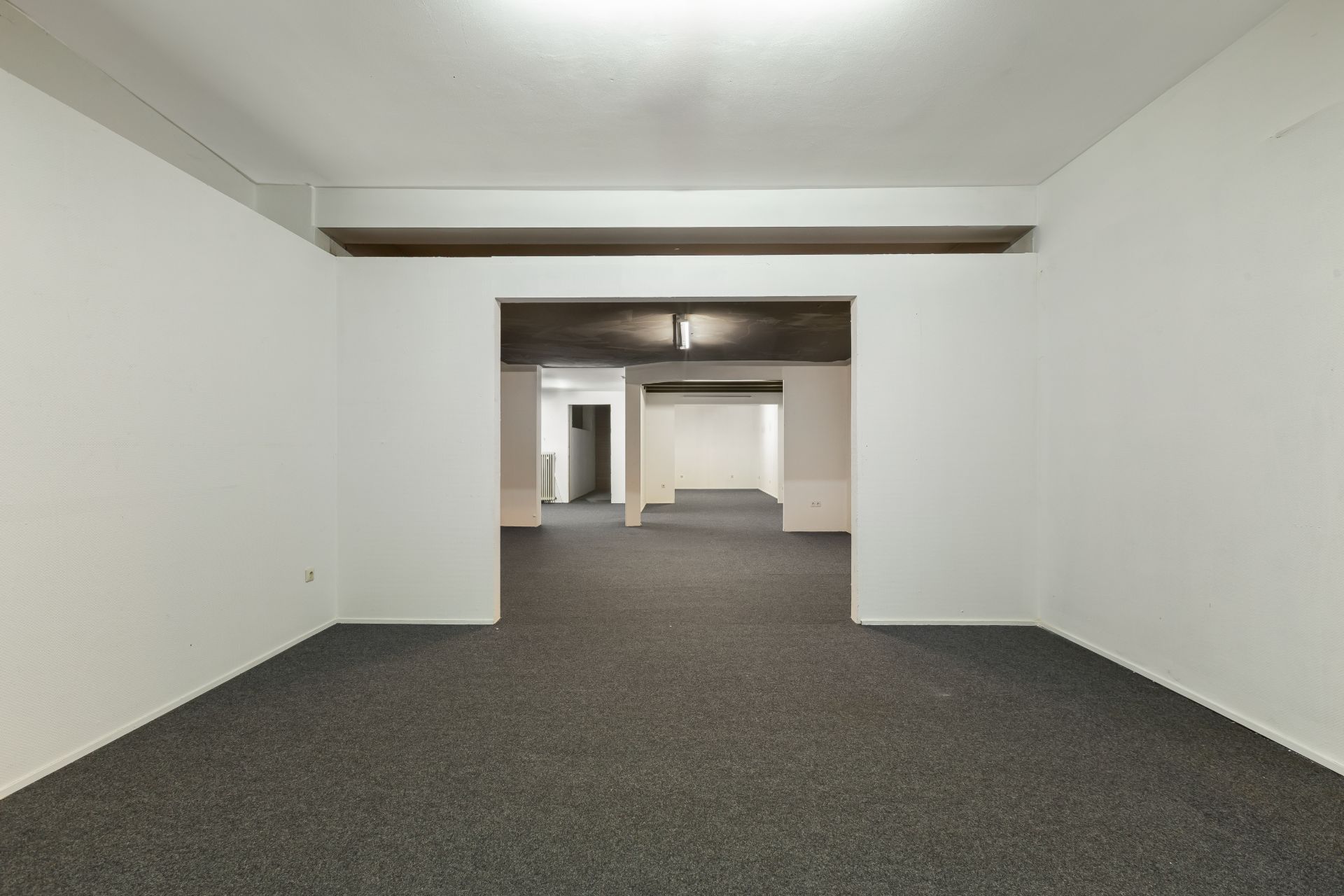 Leerer Raum mit weiß gestrichenen Wänden und grauem Teppichboden.