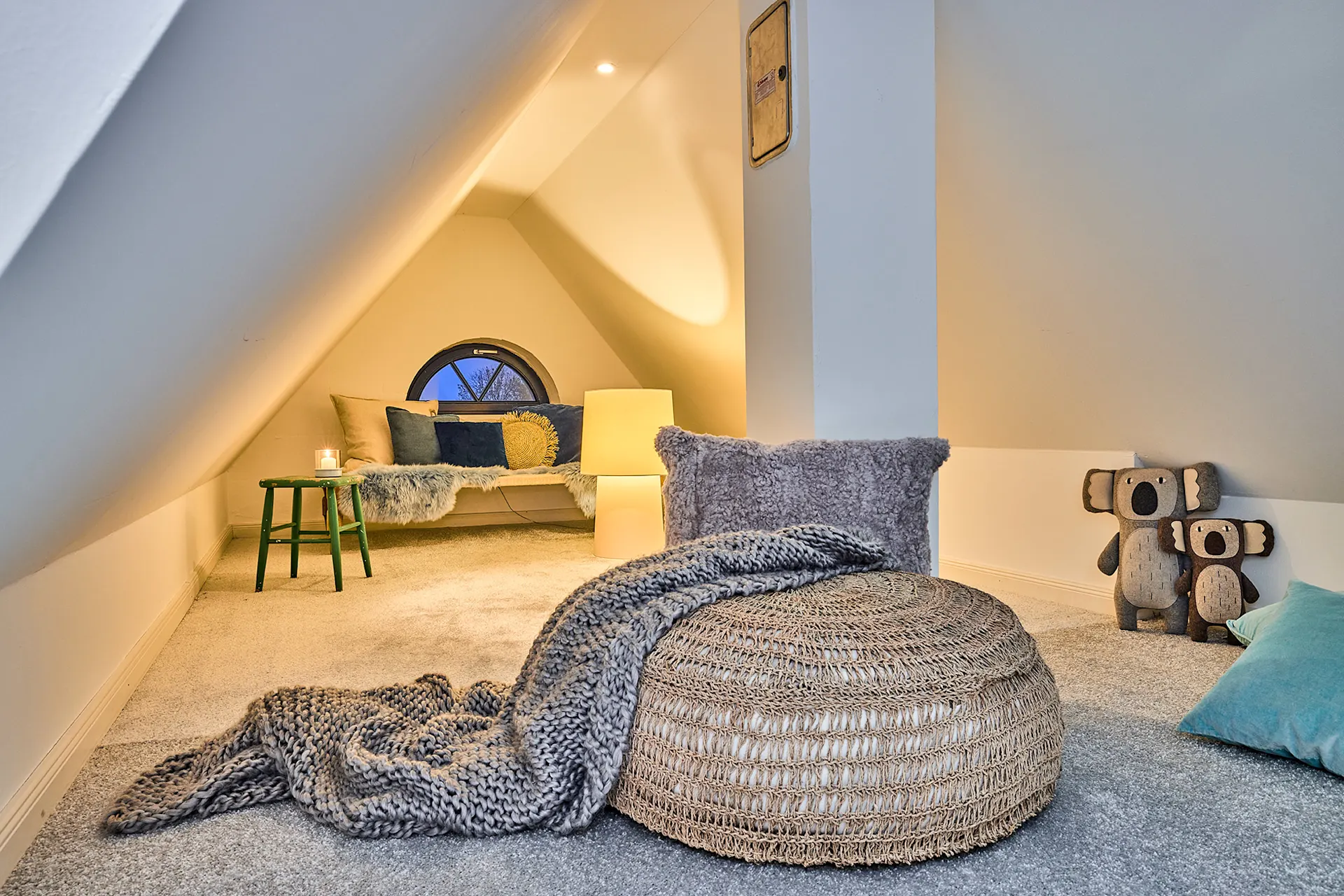 Gemütlicher Dachbodenraum mit Sitzkissen, Kissen, Lampe und zwei Stoff-Koalas.