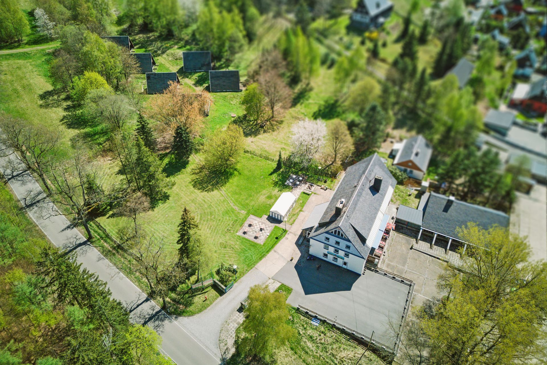 Luftaufnahme eines großen Wohnhauses mit Nebengebäude und mehreren kleinen Hütten im Grünen.
