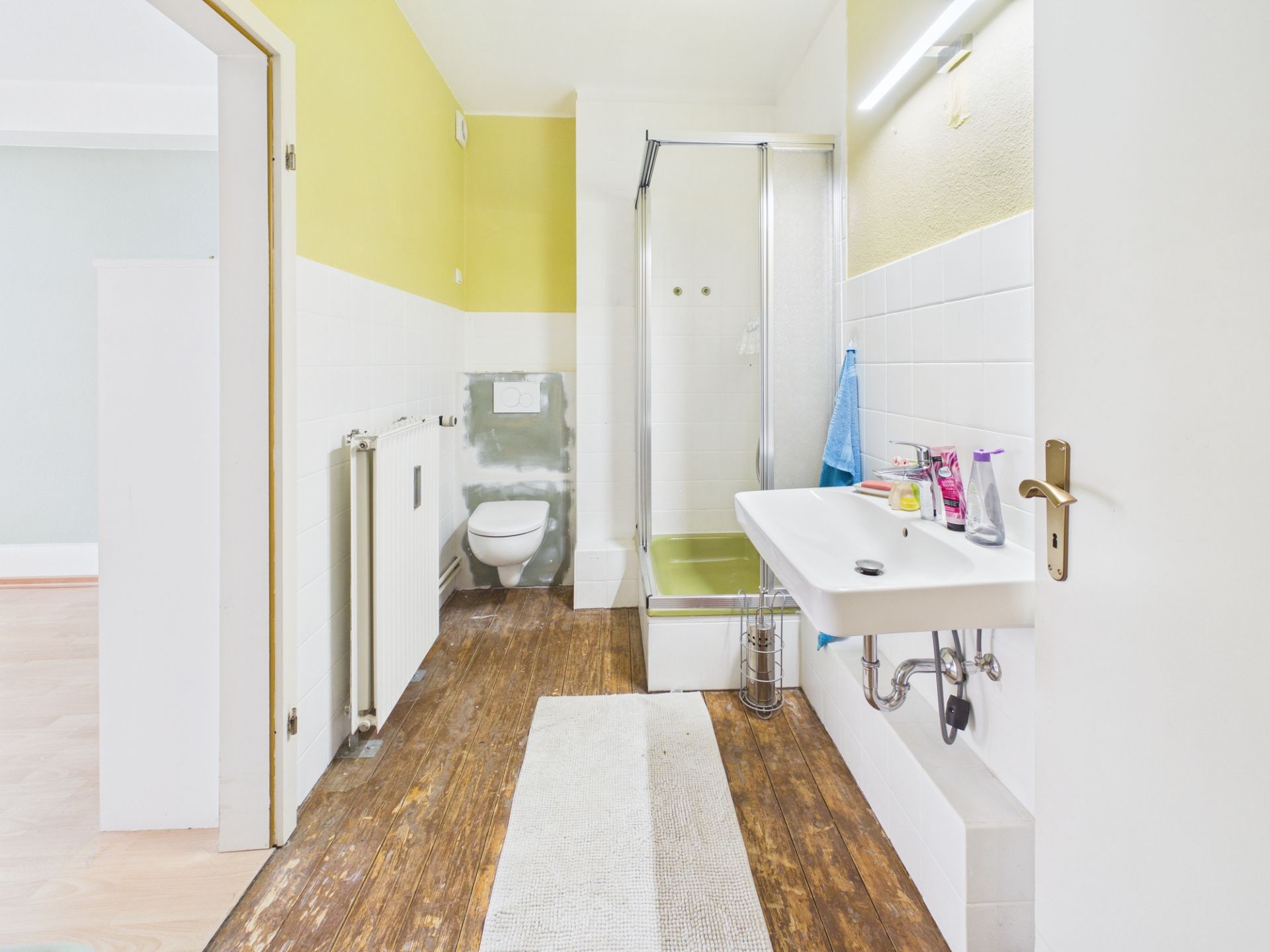 Helles Badezimmer mit Dusche, WC, Waschbecken und Holzfußboden.