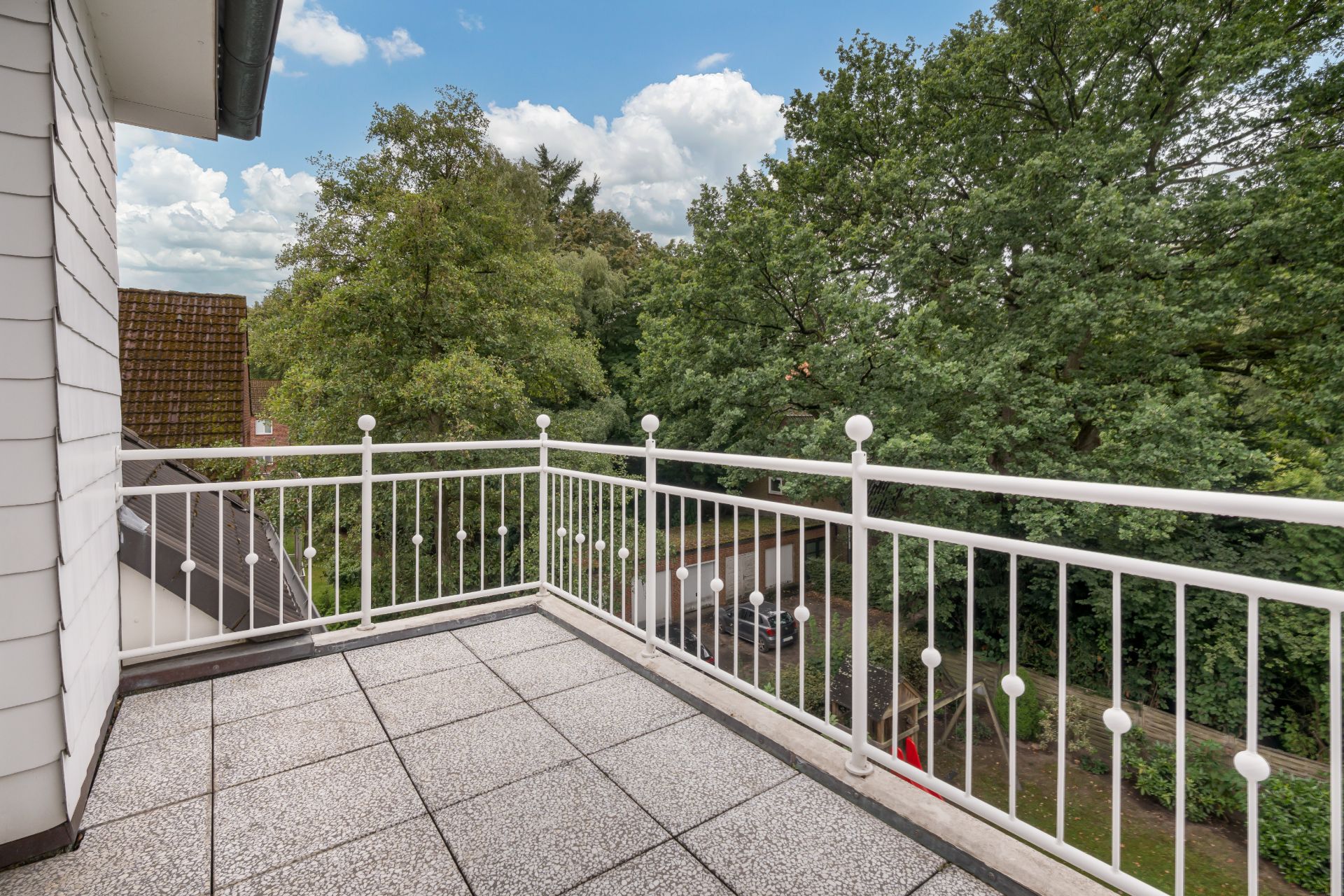 Balkon mit weißem Geländer und Blick auf Bäume und einen Garten.