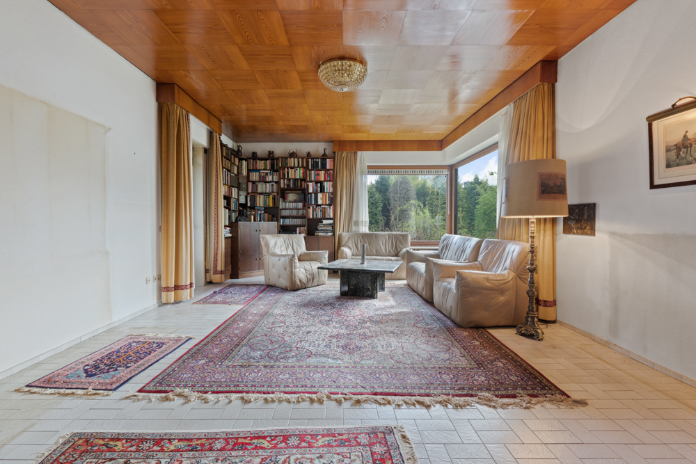 Wohnzimmer mit Ledersofas, Teppichen, Bücherregal, großem Fenster und Kronleuchter.