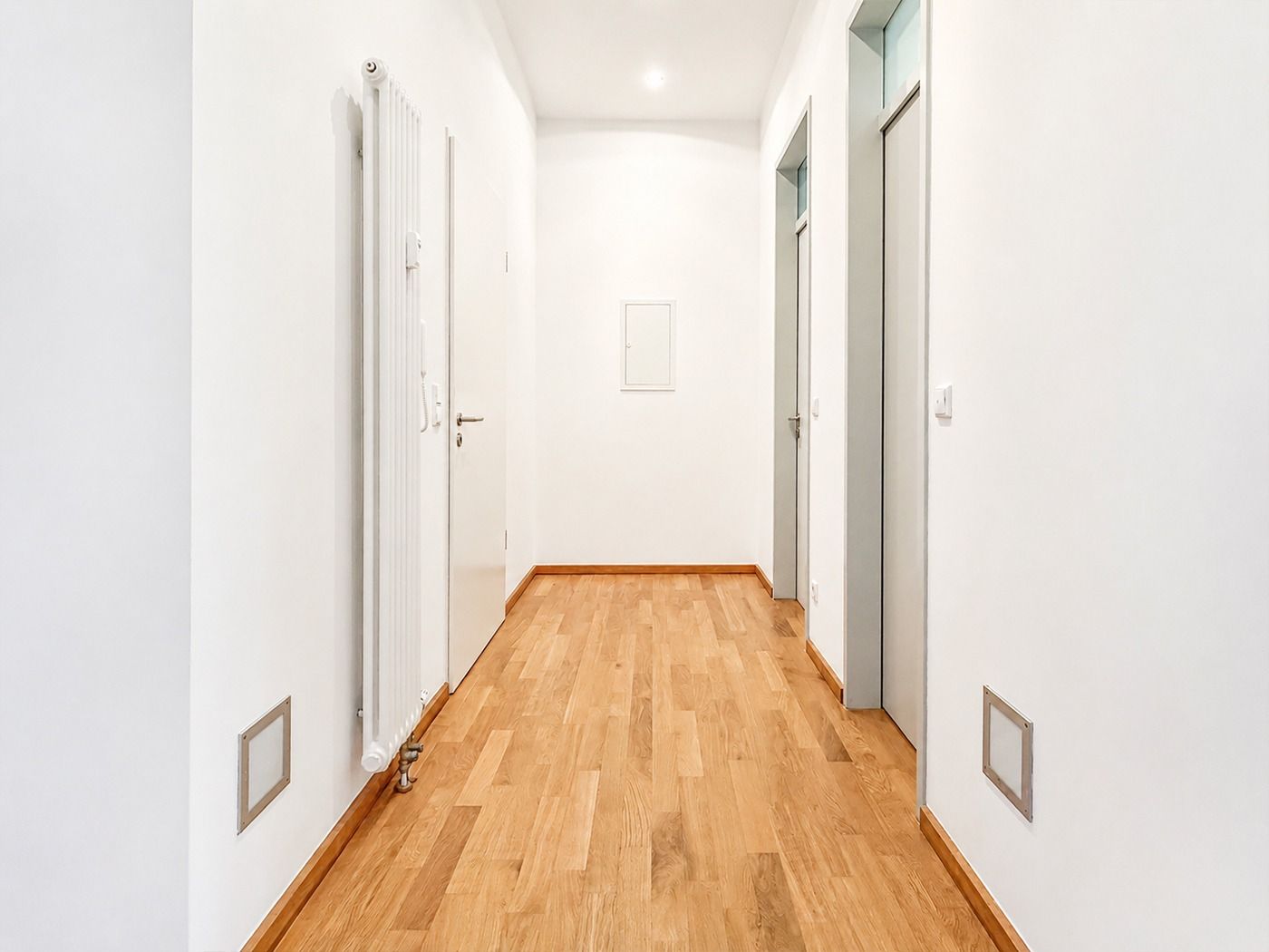 Heller Flur mit Holzboden und weißen Wänden, mehrere Türen an den Seiten.