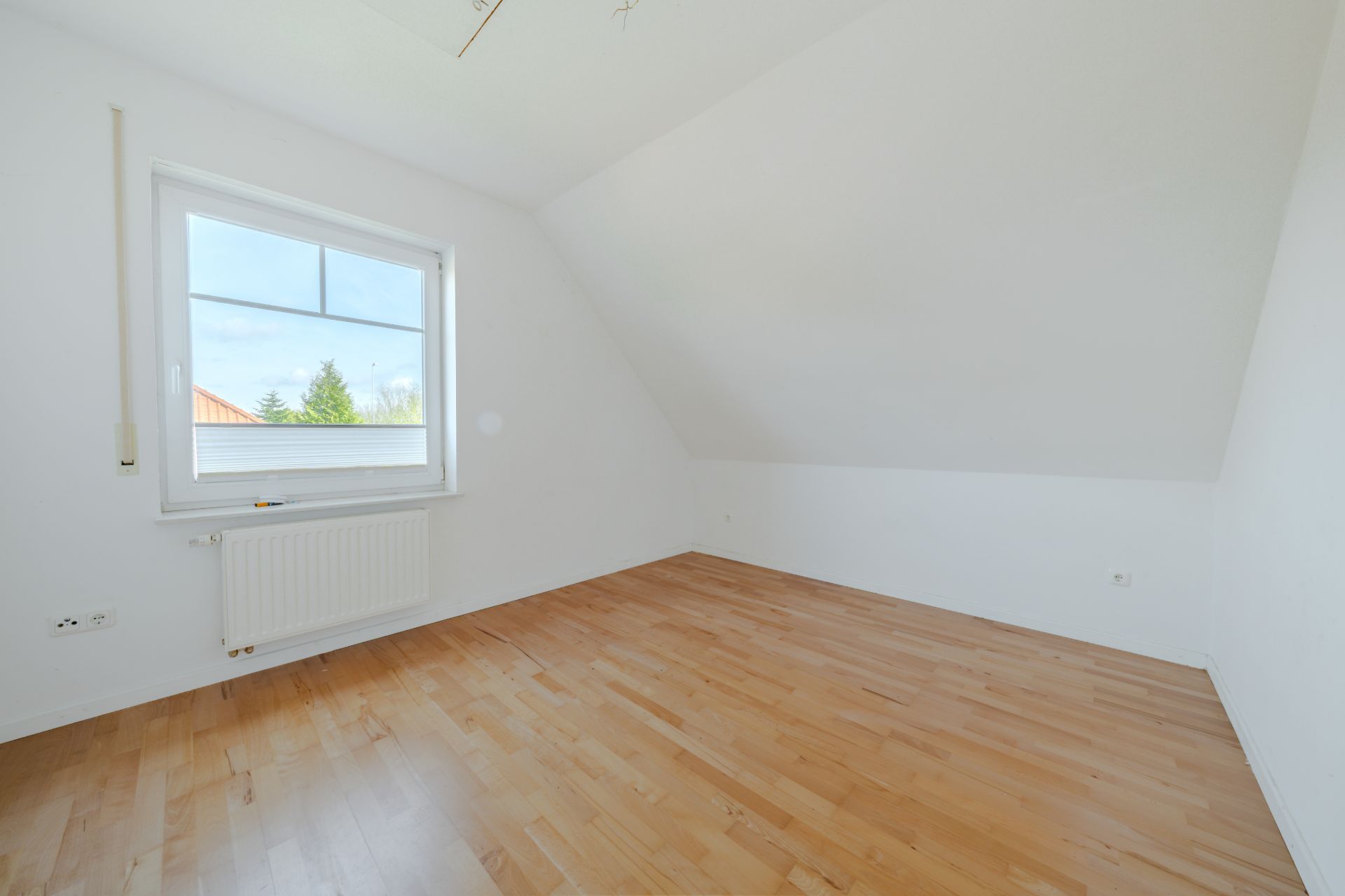 Heller leerer Raum mit Holzfußboden, weiß gestrichenen Wänden und Dachschräge.