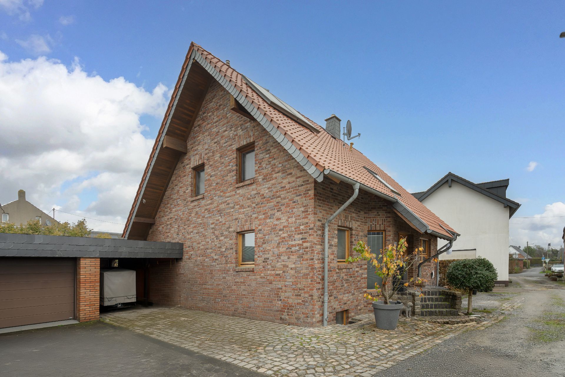 Backsteinwohnhaus mit rotem Satteldach, seitlichem Carport und gepflastertem Hof.