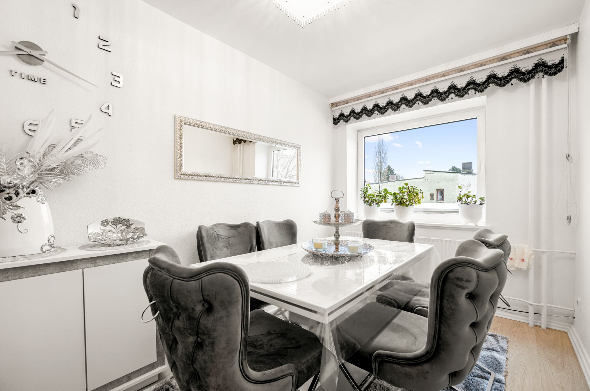 Esszimmer mit sechs gepolsterten Stühlen, weißem Tisch, großem Fenster und Wandspiegel.
