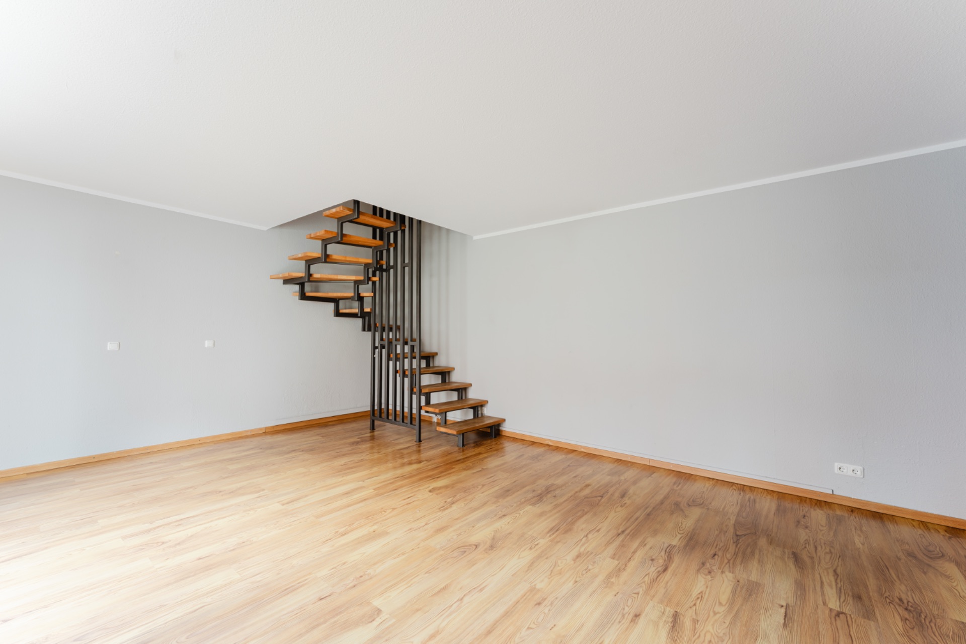 Leerer Raum mit Holzfußboden und moderner, offener Treppe in einer Ecke.