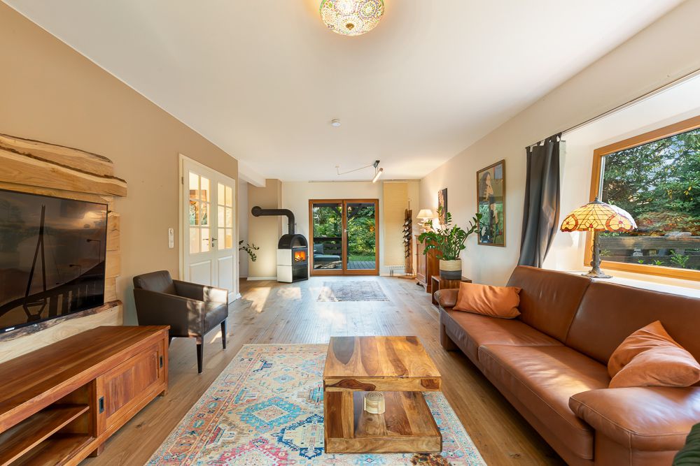 Helles Wohnzimmer mit braunem Sofa, Holztisch, Kamin, großem Fenster und Holzfußboden.