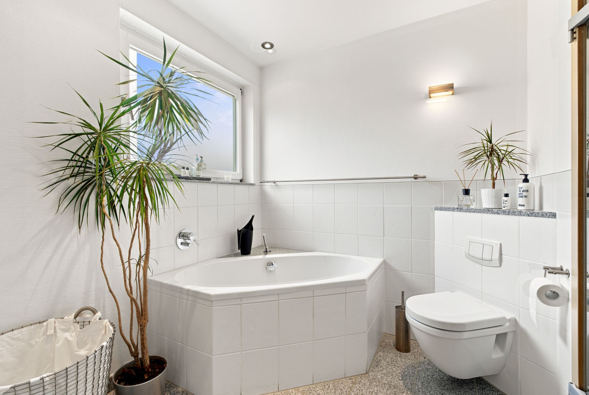 Modernes Badezimmer mit Eckbadewanne, WC, Zimmerpflanzen und Fenster.