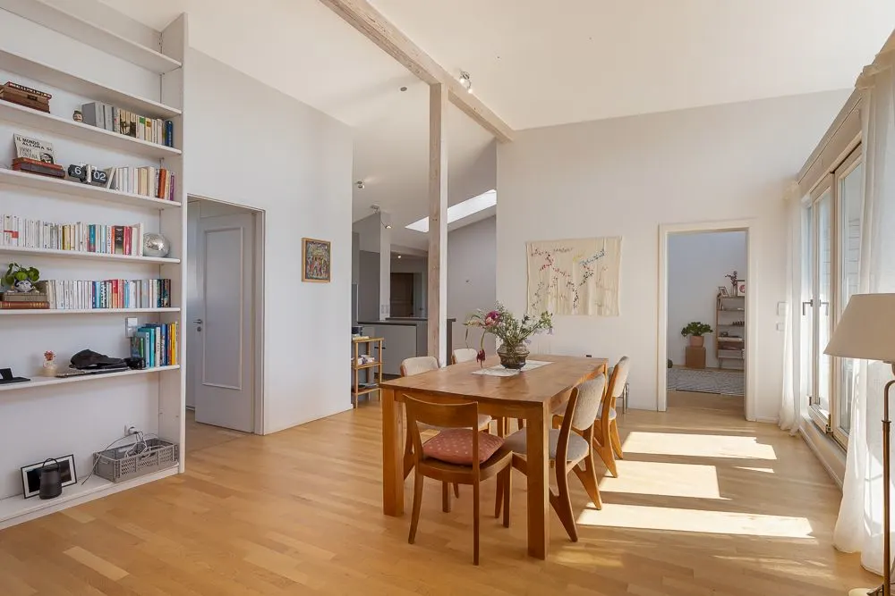 Helles Esszimmer mit Holztisch, sechs Stühlen, Bücherregal und großen Fenstern.