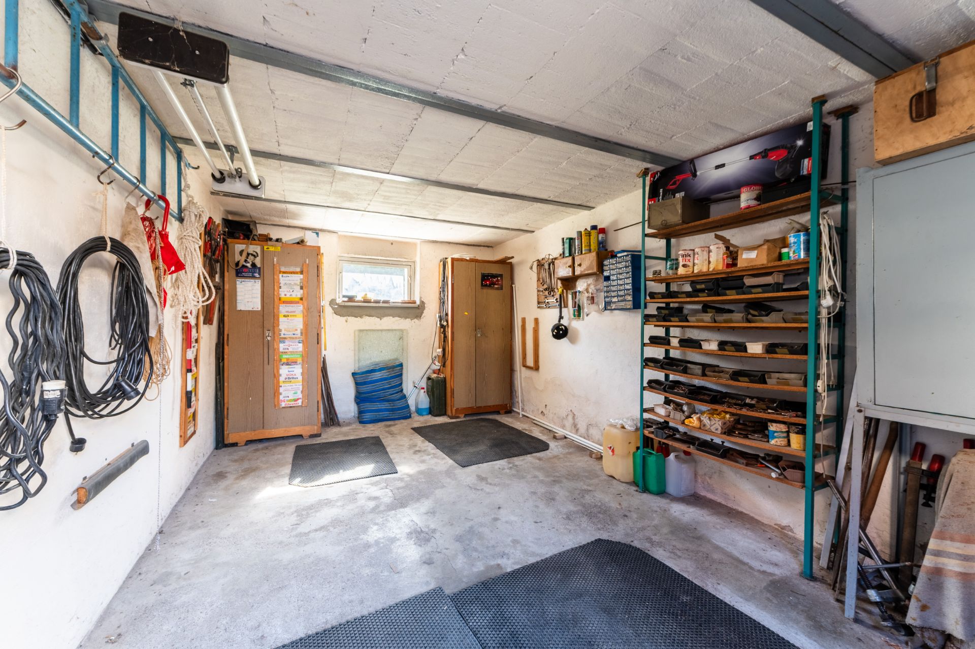 Innenansicht einer Garage mit Regalen, Werkzeugen und aufgerollten Kabeln an den Wänden.