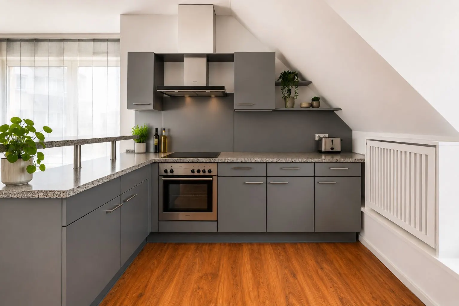 Moderne Küche mit grauen Schränken, Herd, Pflanzen und Holzfußboden unter Dachschräge.
