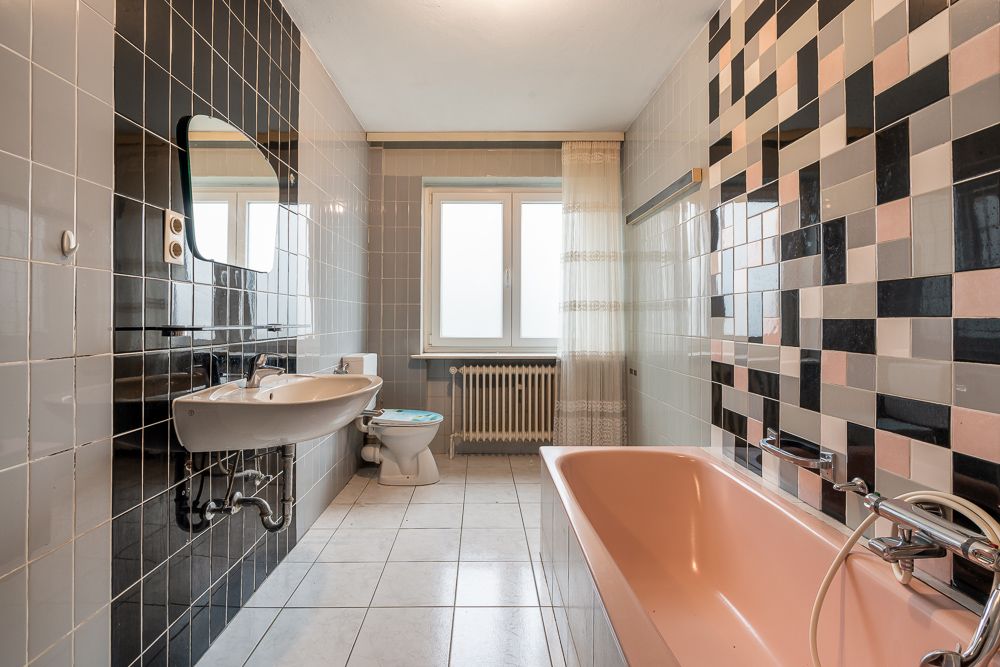 Geräumiges Badezimmer mit rosa Badewanne, Waschbecken, Toilette und gemusterten Wandfliesen.