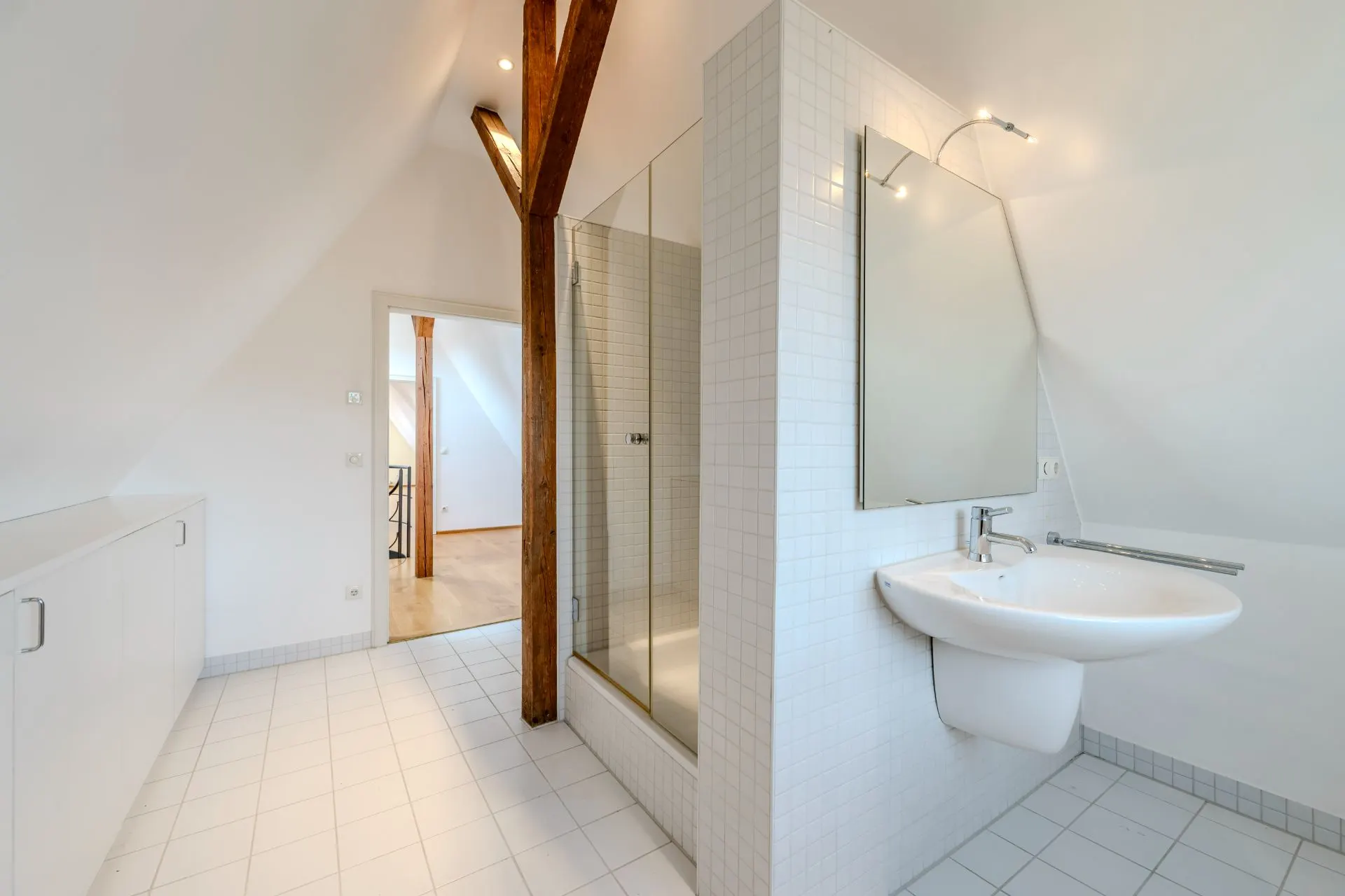 Modernes Badezimmer mit Dusche, Waschbecken, Spiegel und Holzbalken unter dem Dach.