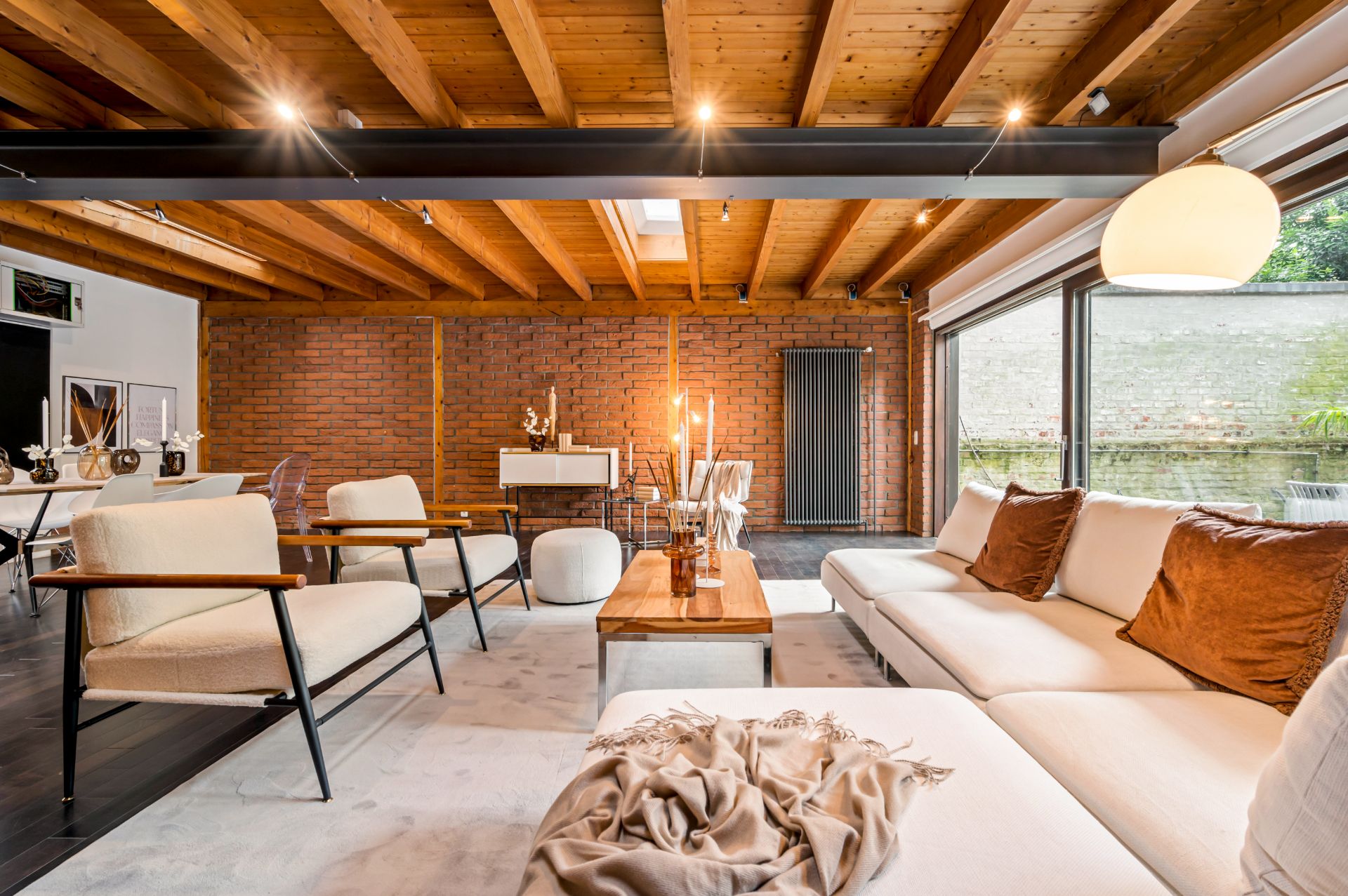 Modernes Wohnzimmer mit Holzdecke, Ziegelwand, Sofas und großen Fenstern zum Garten.
