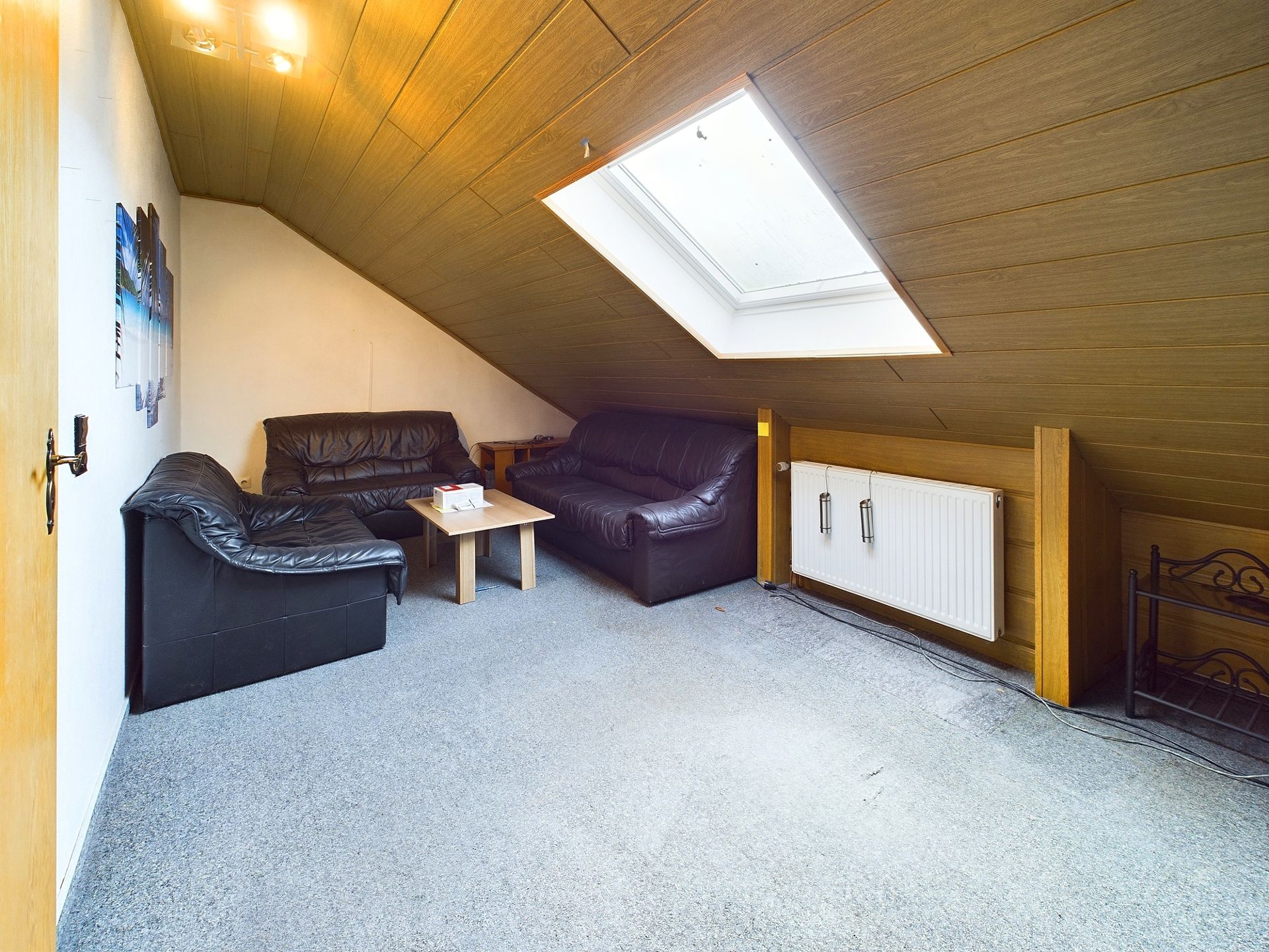 Wohnzimmer mit Dachschräge, zwei schwarzen Sofas, Tisch und Dachfenster.
