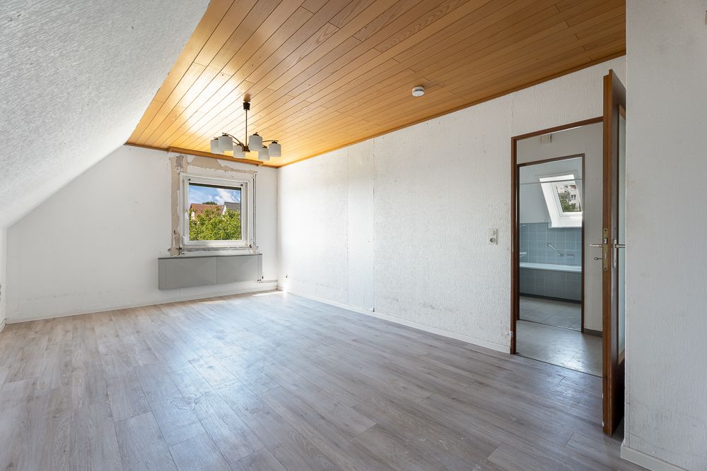 Leerer Raum mit Holzdecke, Fenster, Tür und Zugang zu einem Badezimmer.