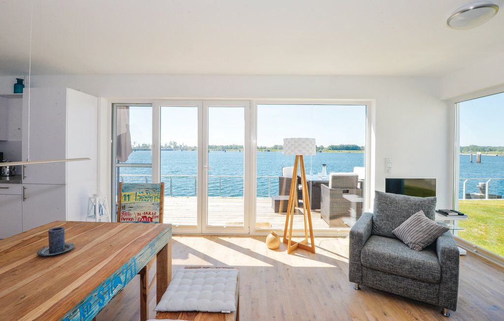 Helles Wohnzimmer mit Sessel, Stehlampe und Blick auf eine Terrasse am Wasser.