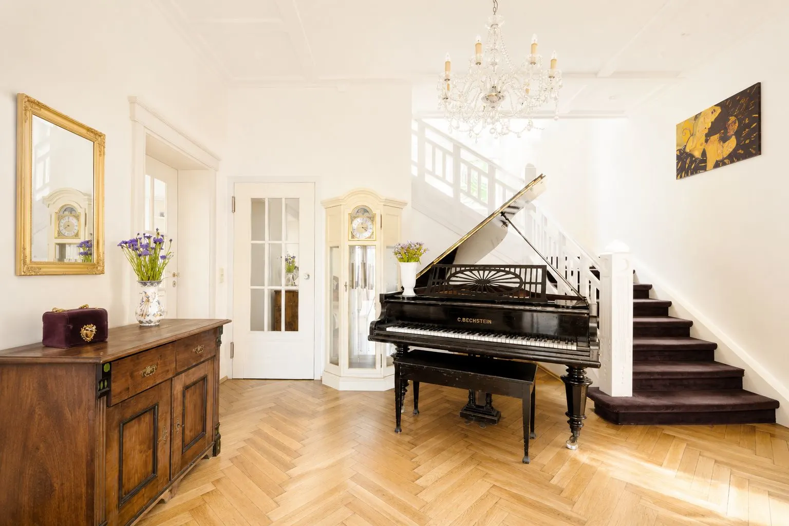 Heller Flur mit Klavier, Holzkommode, Standuhr und Treppe.