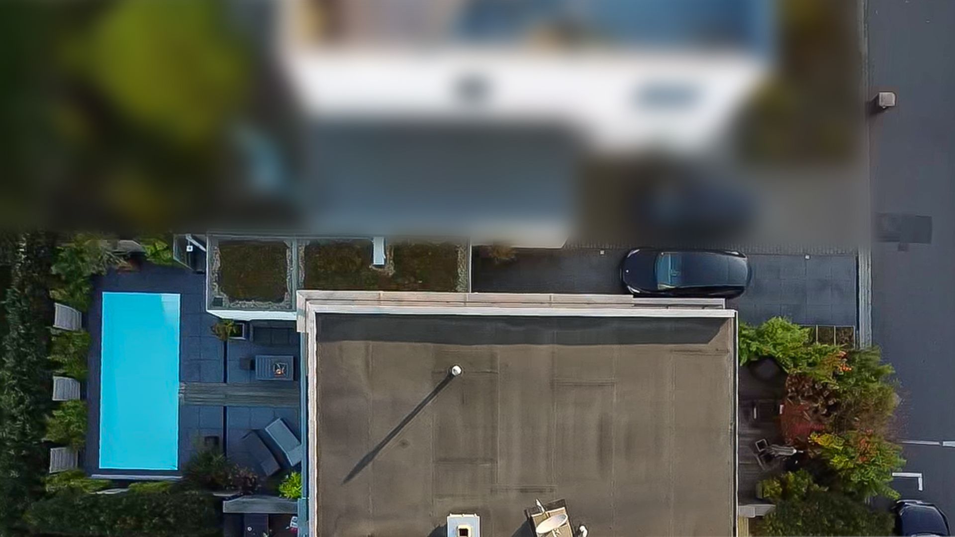 Luftaufnahme eines Wohnhauses mit Flachdach, Terrasse, Pool und geparktem Auto.