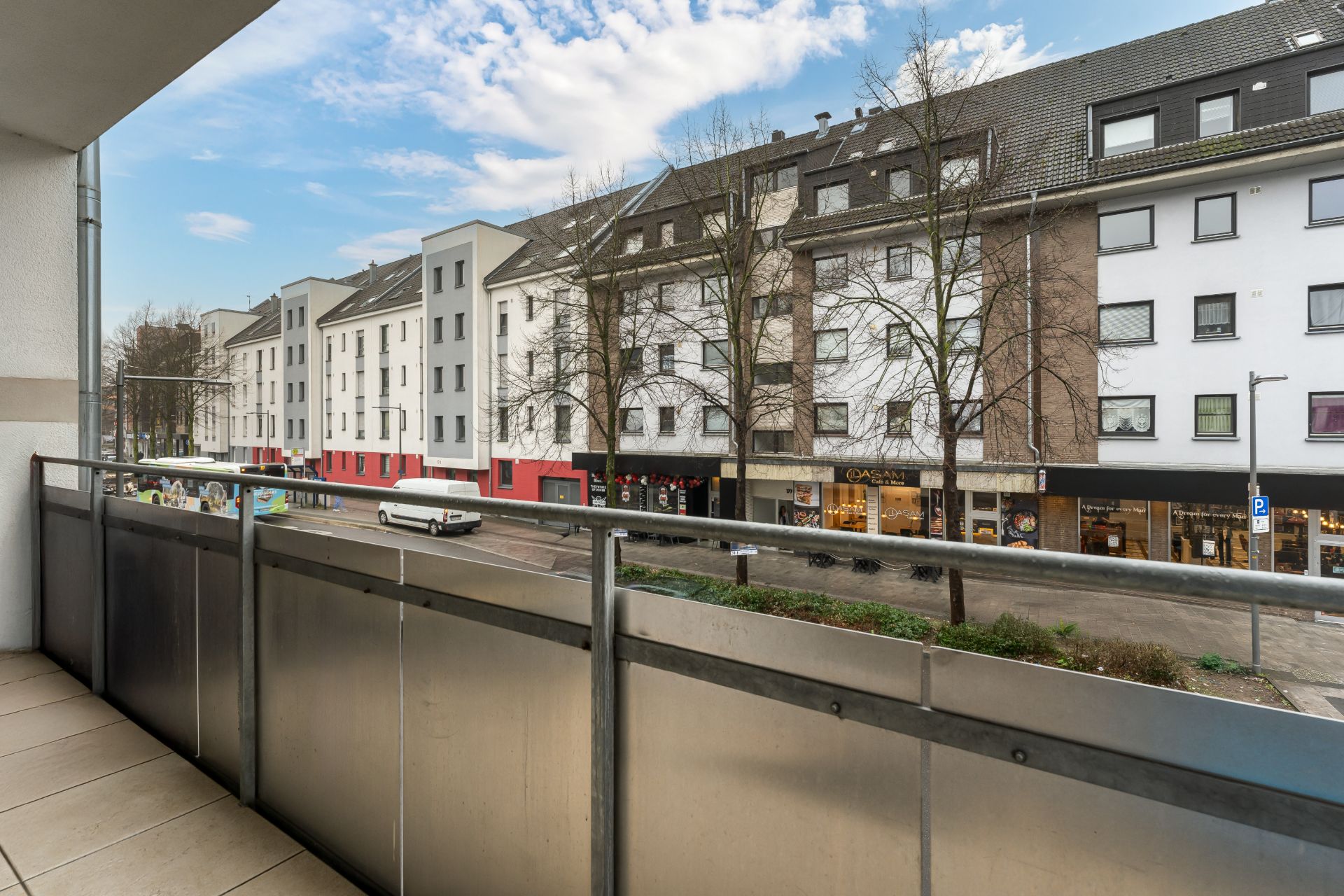 Blick von einem Balkon auf eine Straße mit mehreren Wohngebäuden und Geschäften.