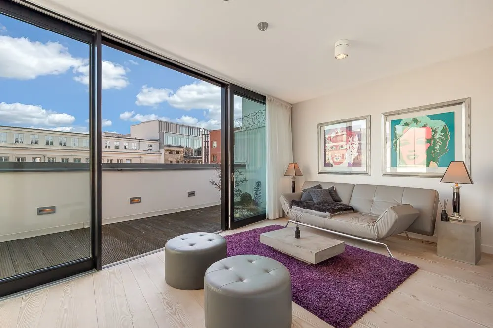 Modernes Wohnzimmer mit Sofa, violettem Teppich und großer Glasfront zu einer Terrasse.