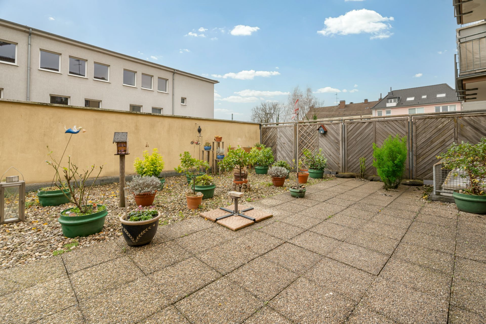Gefliester Innenhof mit mehreren Pflanzkübeln und kleinen Sträuchern, Holzzaun im Hintergrund.