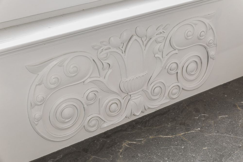 Weiße, dekorative Stuckverzierung an einer Wand mit floralen und geschwungenen Mustern.