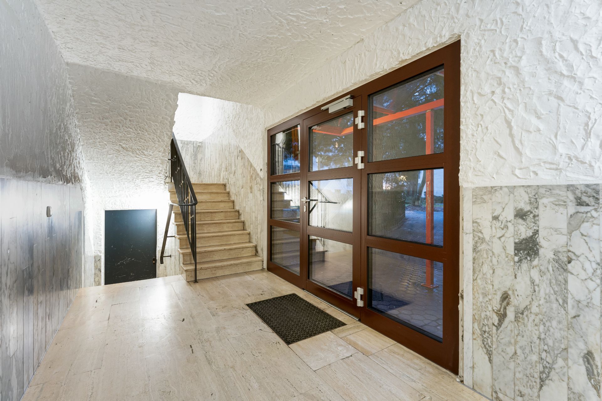 Eingangsbereich mit Glastür, Marmorboden und Treppe in einem Wohngebäude.