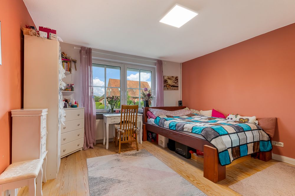 Helles Schlafzimmer mit großem Bett, Schreibtisch am Fenster und oranger Wand.