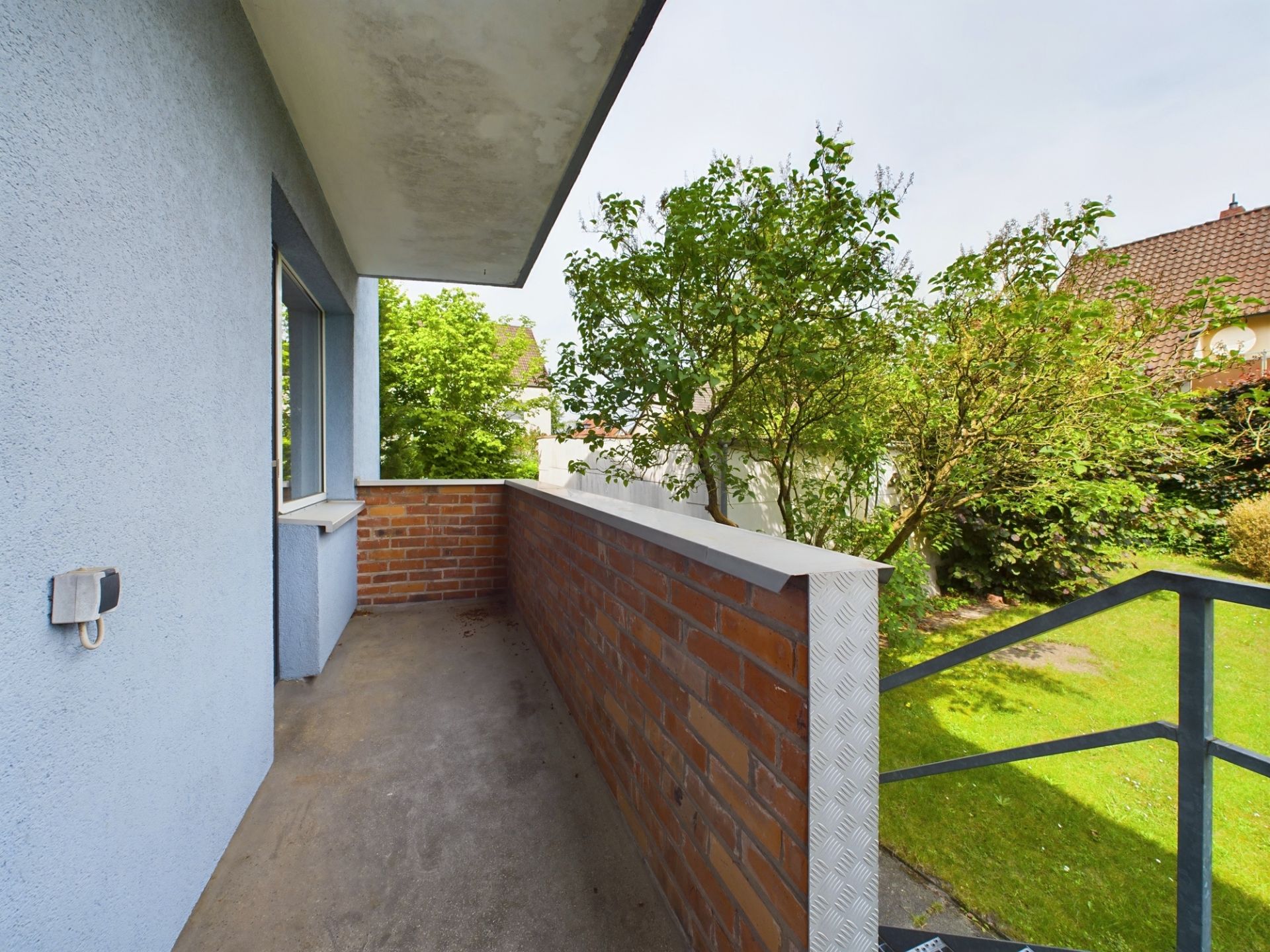 Kleiner Balkon mit Backsteinmauer und Blick auf einen grünen Garten mit Bäumen.