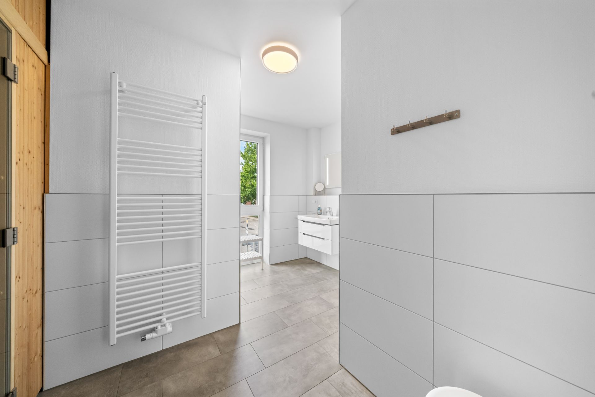 Modernes Badezimmer mit weißem Handtuchheizkörper und großem Fenster.