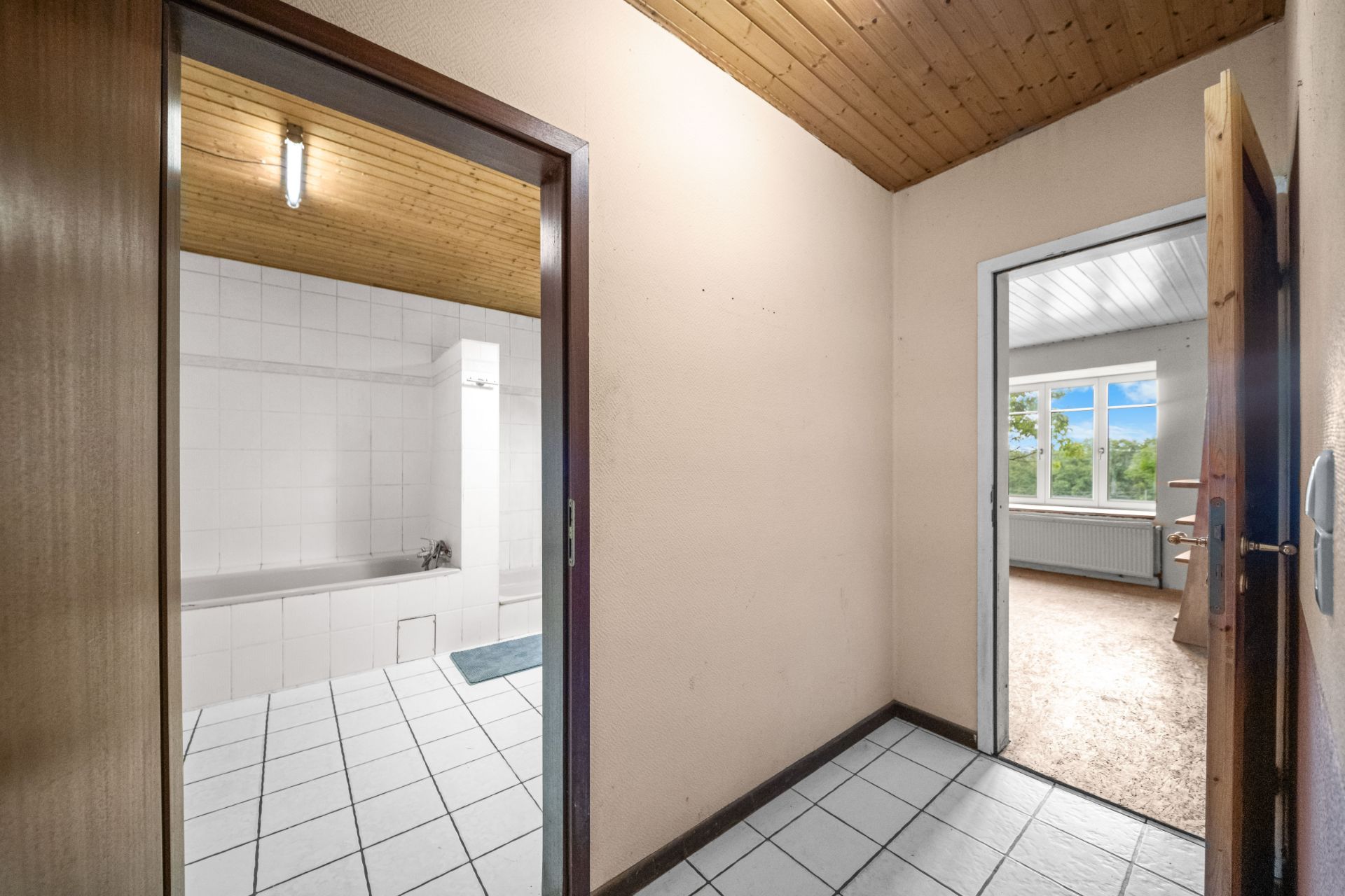Flur mit Zugang zu einem gefliesten Badezimmer und einem Raum mit großem Fenster.