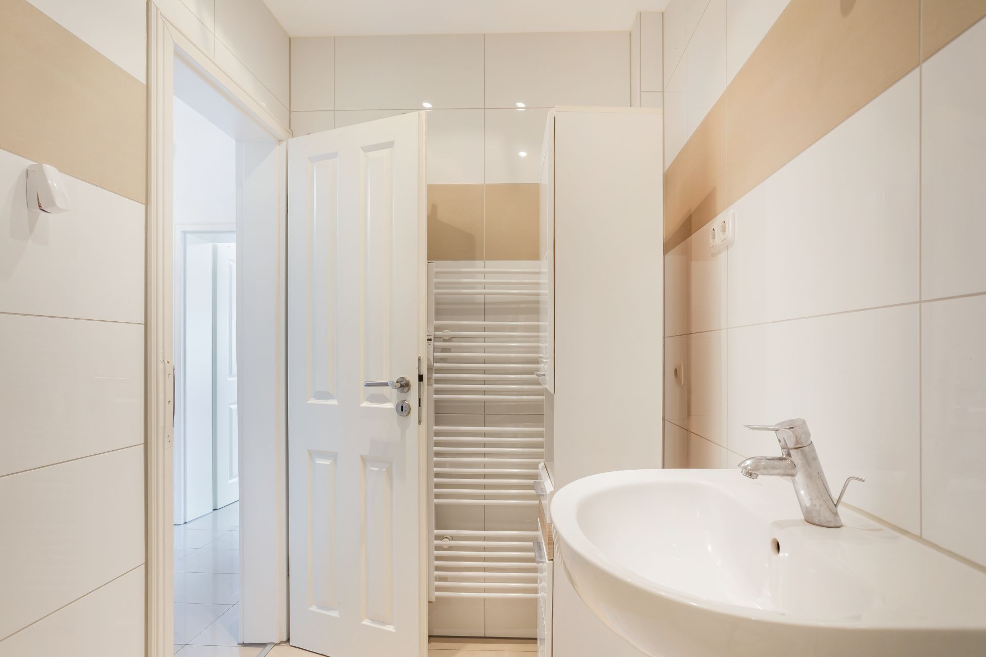 Helles Badezimmer mit Waschbecken, Handtuchheizung und offener Tür.