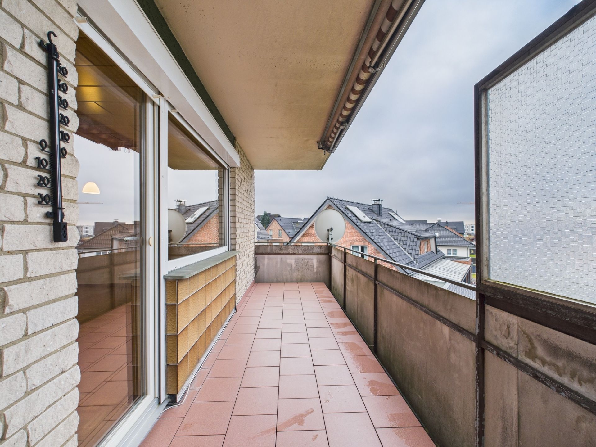 Überdachter Balkon mit Fliesenboden, Geländer und Blick auf Nachbarhäuser.
