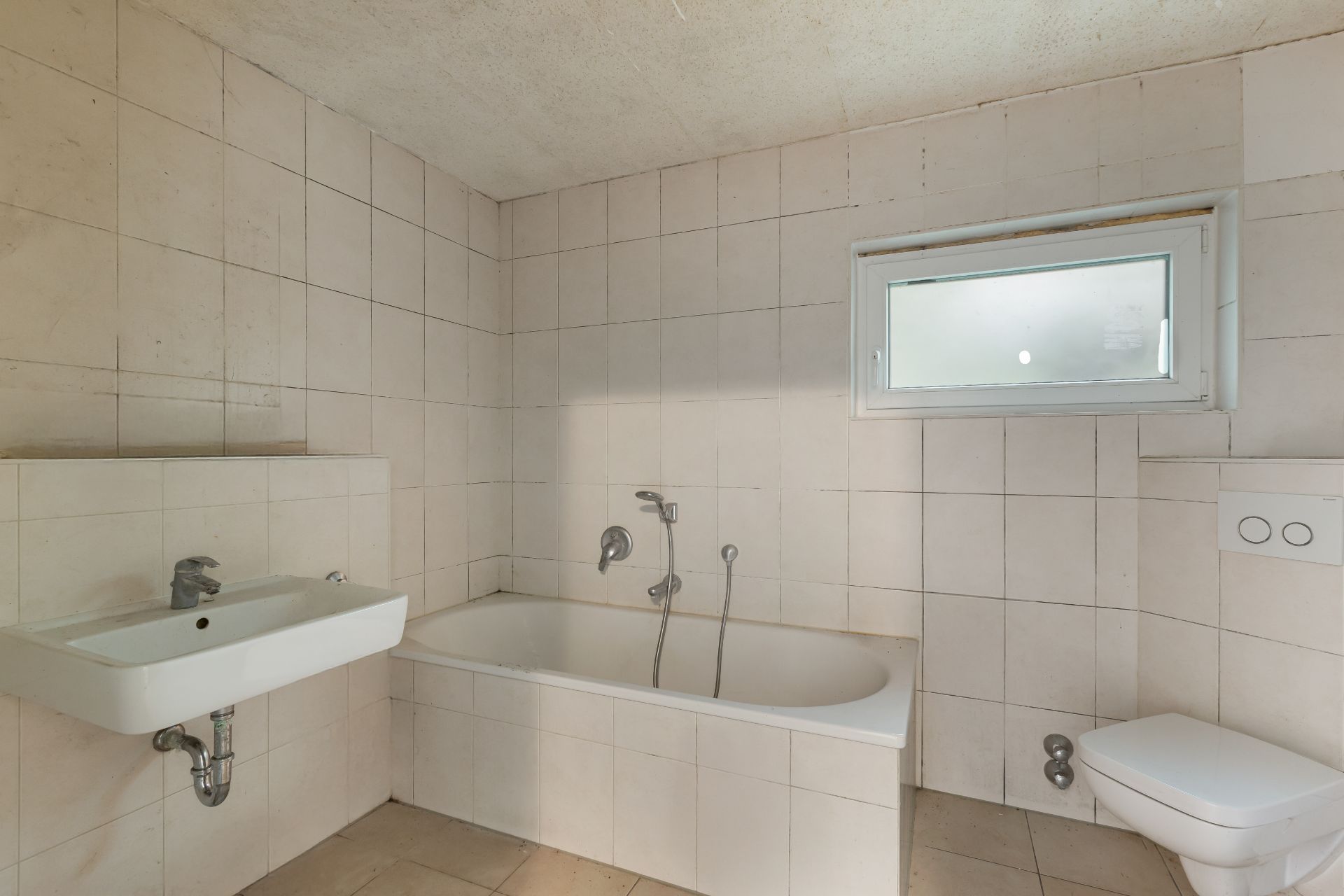 Helles Badezimmer mit Badewanne, Waschbecken, Toilette und kleinem Fenster.