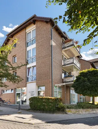 Mehrstöckiges Wohnhaus aus Backstein mit Balkonen, Bäumen und Gehweg im Vordergrund.