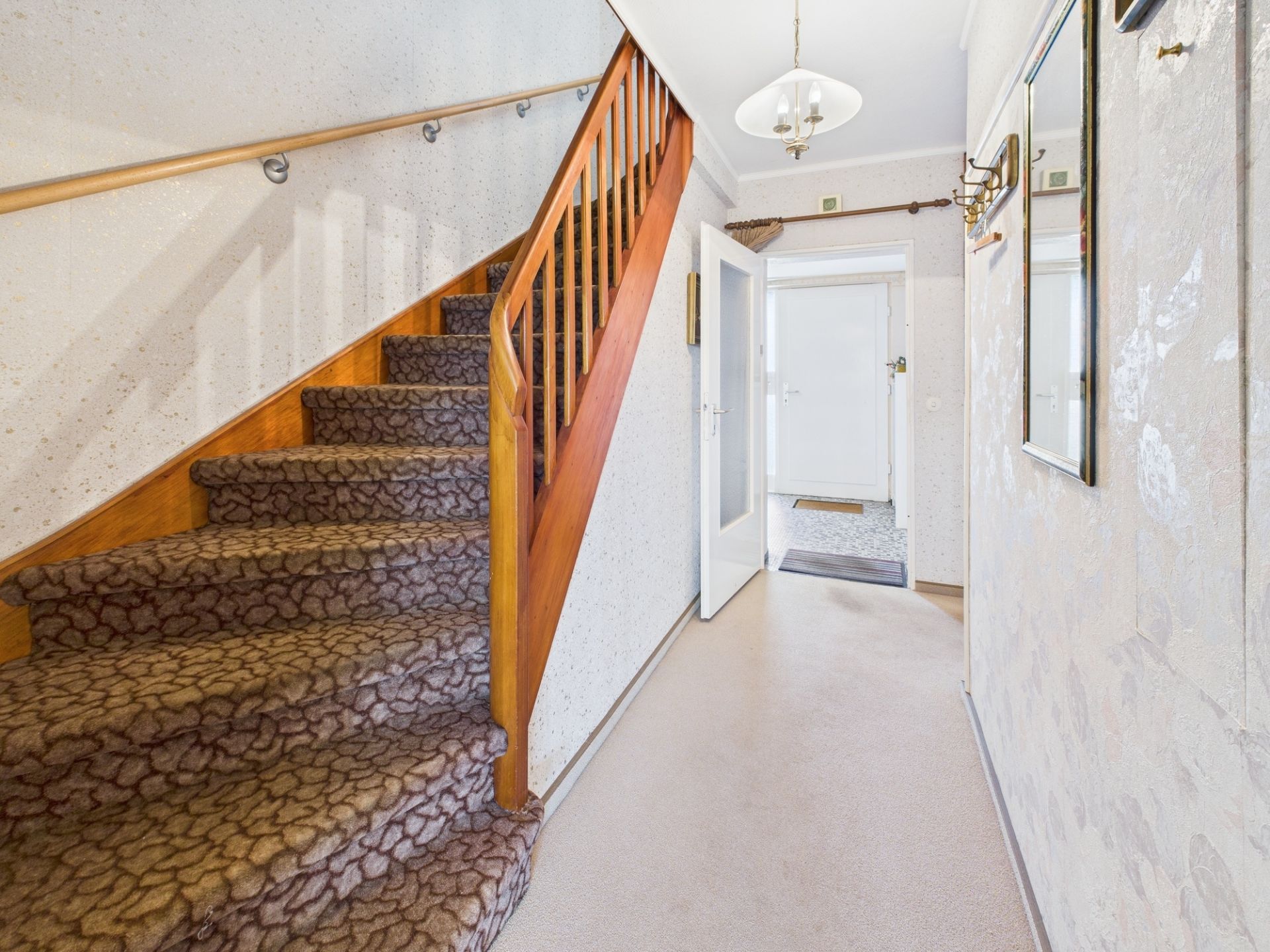 Heller Flur mit Teppichtreppe und Holzgitter, Spiegel an der Wand und Deckenlampe.