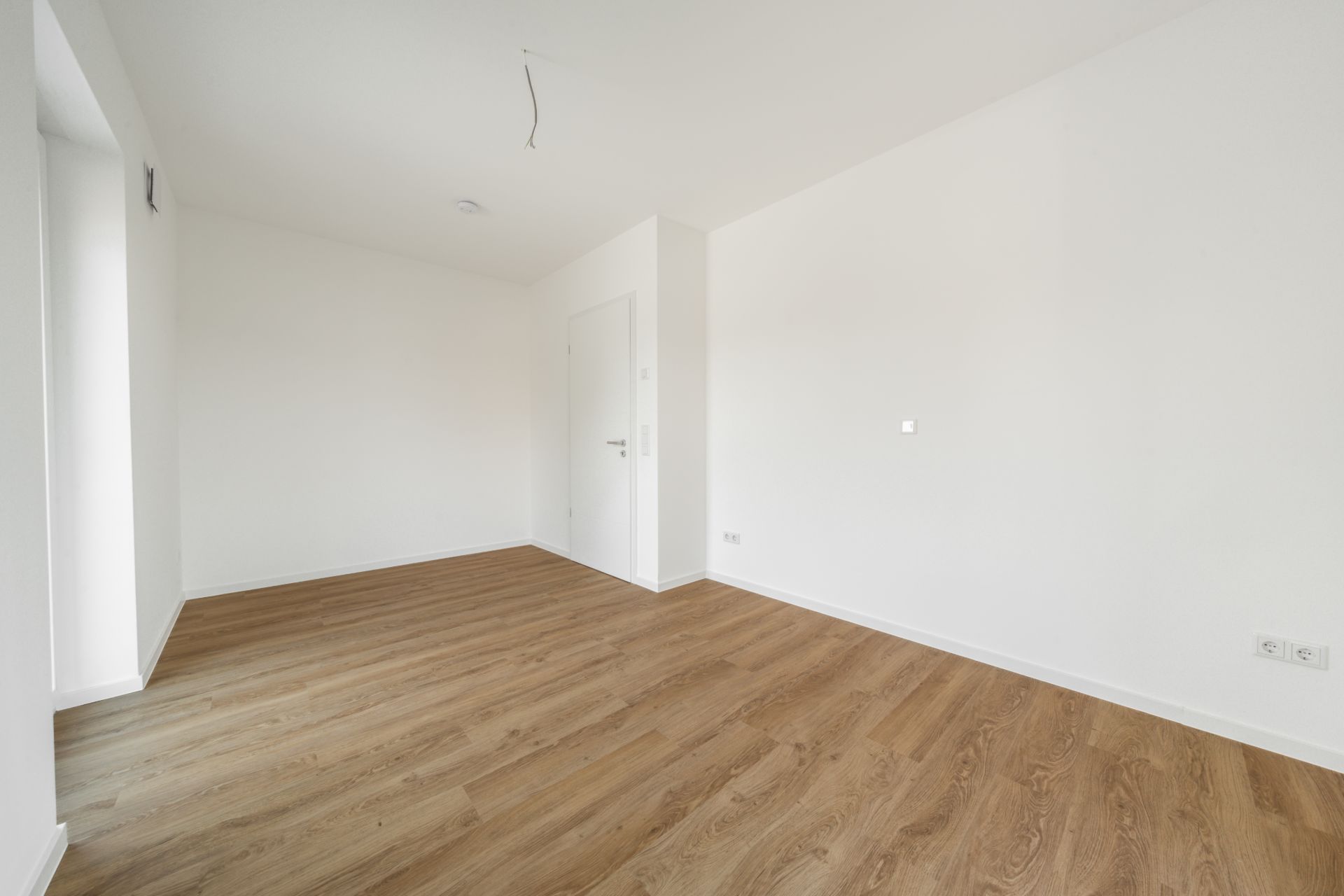 Leerer Raum mit weiß gestrichenen Wänden und hellem Holzboden.