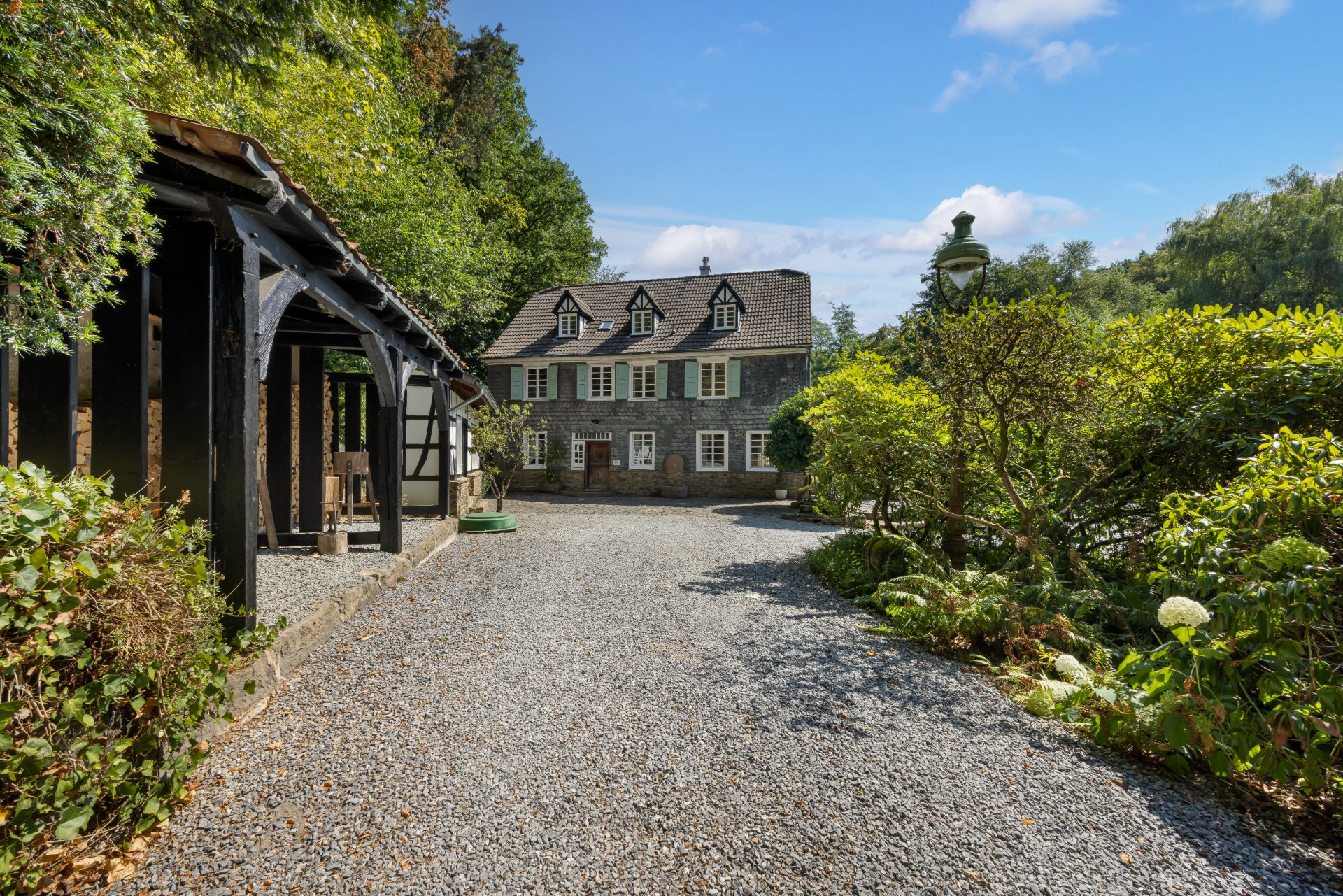 Großes Wohnhaus mit Schieferfassade, Kiesweg, Garten und überdachtem Bereich im Vordergrund.