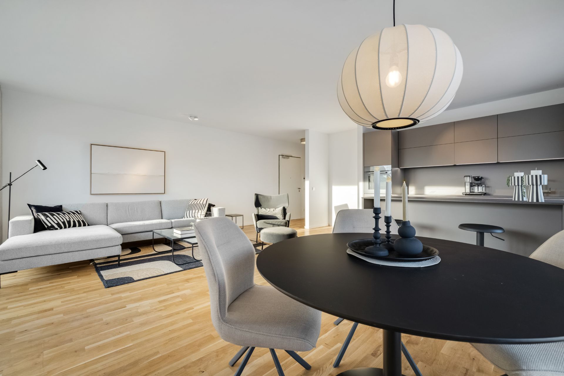 Modernes Wohnzimmer mit offener Küche, Esstisch und grauem Sofa auf Holzfußboden.